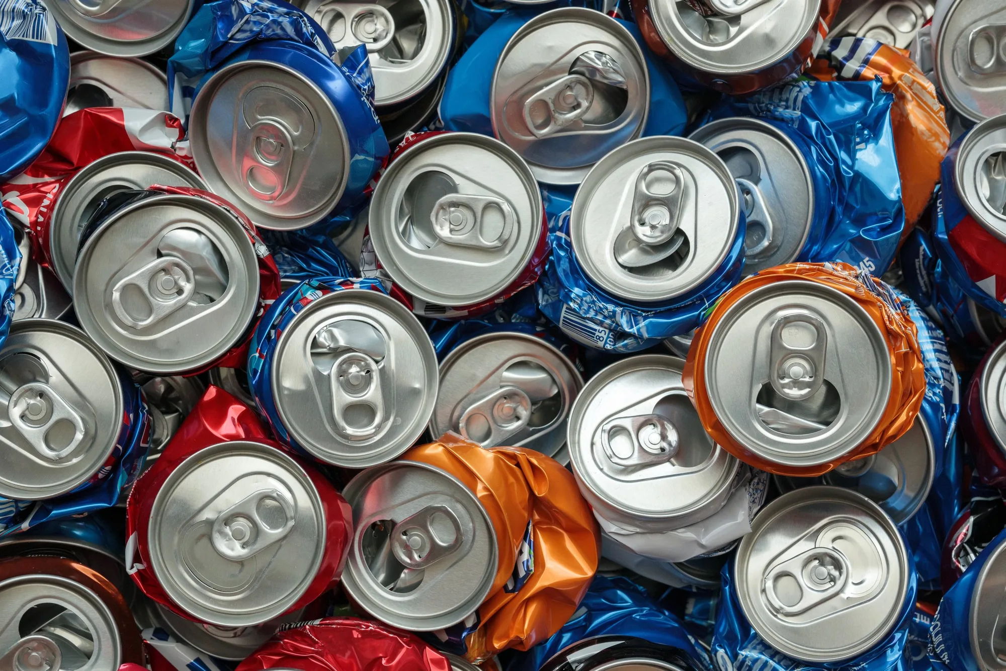 A large pile of crushed aluminum cans in red, blue, orange, and silver colors.